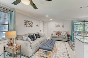 A modern living room with a sofa, ottoman, and a coffee table. There is a dining area with a table and chairs. - *Upscale 2/2 condo with pool 6 mins from IMG (Bradenton)