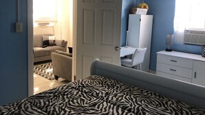 Un dormitorio con una cama, un escritorio, una silla, un armario y una puerta que da a otra habitación.