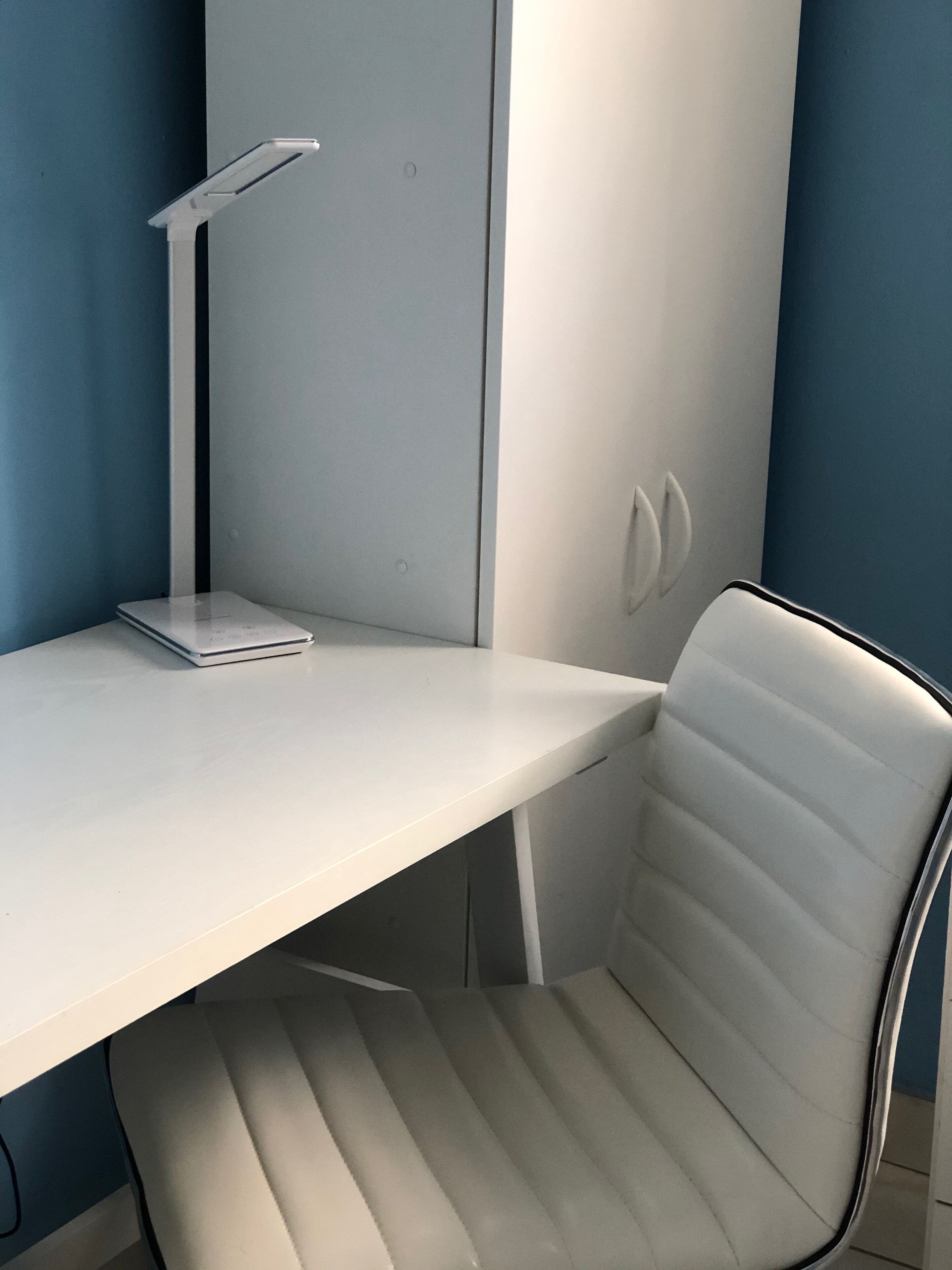 A modern office desk with a laptop, a white chair, and a desk lamp.