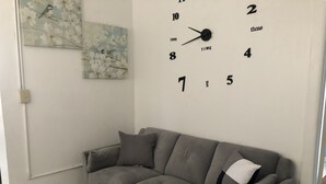 Una sala de estar con un sofá gris, un reloj de pared y un cuadro con motivos florales.