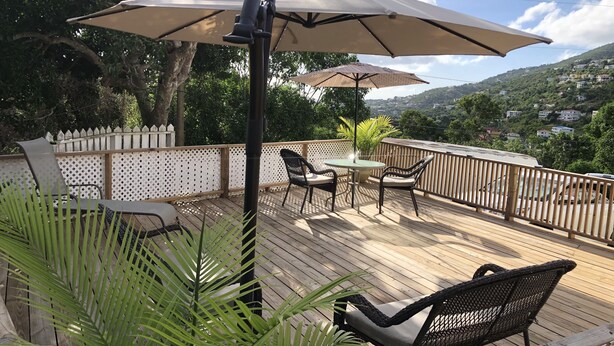 Una terraza de madera con mobiliario exterior, incluyendo sillas y una mesa, bajo un paraguas grande.