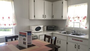 Cocina compacta con armarios blancos, microondas, tostadora y pileta.