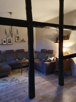 Una sala de estar acogedora con techo de madera oscura, una araña, un conjunto de sofás, una mesa de centro y un mueble de madera pequeño.