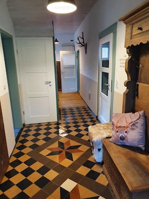 Un pasillo con piso a cuadros, una puerta blanca y un armario de madera con cuernos de ciervo.