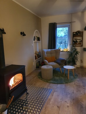 Una sala de estar acogedora con una estufa de leña, un sofá cómodo, una mesita redonda y una estantería.