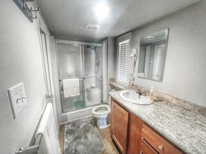 Ein Badezimmer mit Glasdusche, Toilette, Waschbecken mit Spiegel und Holzschränken.