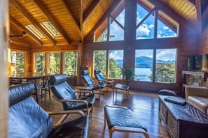 A wooden cabin with large windows offering mountain views, leather seating, and a wooden dining table. - Thimbleberry Bay House (Sitka)