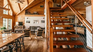 A spacious wooden interior with a high ceiling, a staircase, and a dining area.