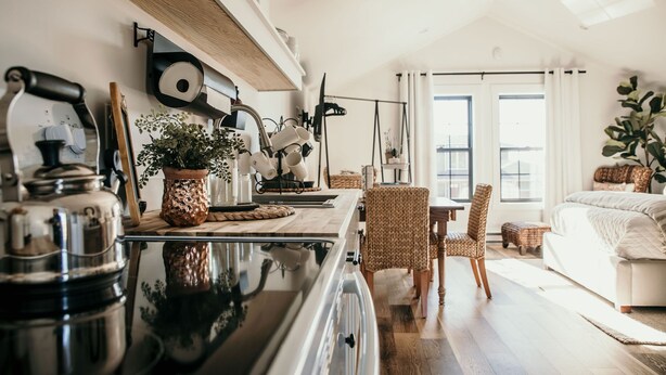 A modern kitchen with a large stove, wooden cabinets, and a dining area with wicker chairs. - 738 Alice Loop - 4 Sea's Cottage (Sitka)