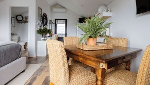 A dining area with a wooden table and woven chairs, a potted plant, and a view into the adjacent living room. - 738 Alice Loop - 4 Sea's Cottage (Sitka)
