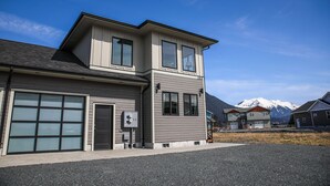 A two-story house with a garage, a small porch, and a mountain backdrop. - 730 Alice Loop: 3  BR, 2  BA Duplex in Sitka, Sleeps 6 (Sitka)