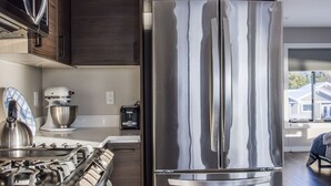 A modern kitchen with stainless steel appliances, dark wooden cabinets, and a large window providing natural light. - 730 Alice Loop: 3  BR, 2  BA Duplex in Sitka, Sleeps 6 (Sitka)