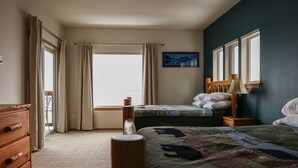 A bedroom with a large window, a bed, a dresser, and a nightstand. - Admiralty Suite at Island View (Sitka)