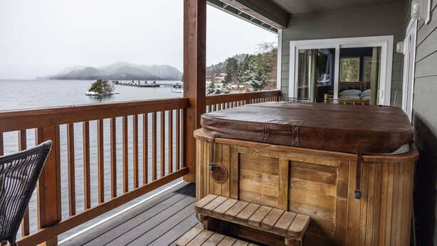 A wooden hot tub on a deck with a view of a lake and mountains. - Admiralty Suite at Island View (Sitka)