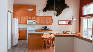 A modern kitchen with wooden cabinets, a central island, and a hanging light fixture. - Admiralty Suite at Island View (Sitka)