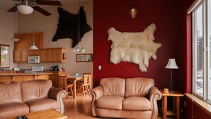 A living room with leather sofas, a dining area, a kitchen, and a large window with a view. - Admiralty Suite at Island View (Sitka)