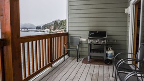 Een balkon met een barbecue en stoelen, met uitzicht op een waterpartij en bergen.