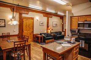 Un espacio de sala acogedor con una mesa de comedor de madera, un sofá de cuero negro y una cocina con armarios de madera y un horno negro.