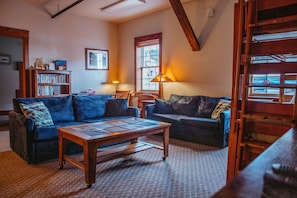 A cozy living room with two dark blue sofas, a wooden coffee table, and a bookshelf.