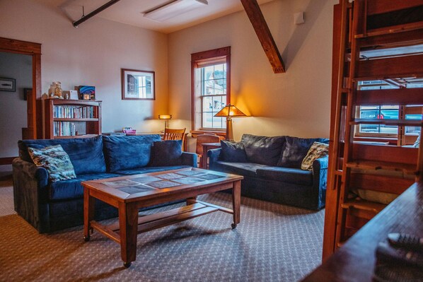 A cozy living room with two dark blue sofas, a wooden coffee table, and a bookshelf.