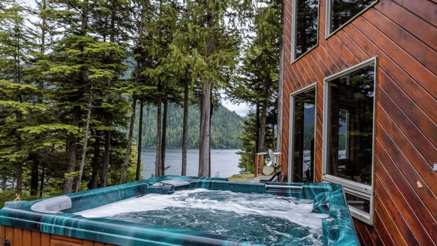 Un bain à remous à motifs écossais, entouré d’une terrasse en bois et offrant une vue sur un lac bordé de forêts.