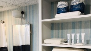 Un bany amb un lavabo, un mirall i prestatges amb tovellons i productes de tocador.