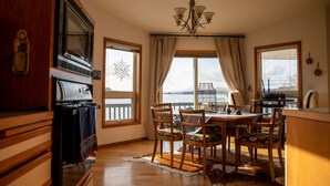 Un espace repas comprenant une table en bois, des chaises et une vue sur une étendue d’eau, grâce à de grandes fenêtres.