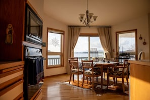 A dining area with a wooden table, chairs, and a view of a body of water through large windows.