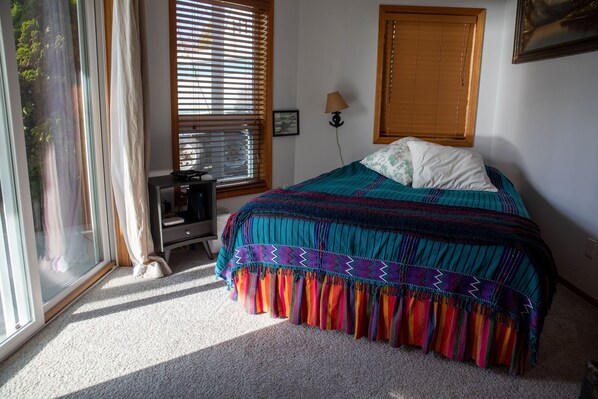 A bedroom with a bed, a desk, a lamp, and a window with blinds.
