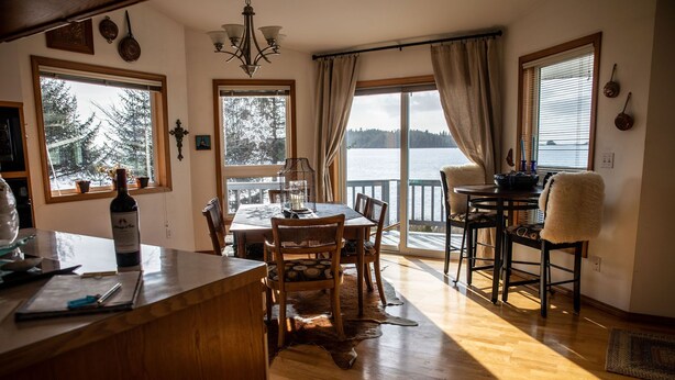 Un coin repas chaleureux, avec des meubles en bois, une grande fenêtre donnant sur un lac et un tapis rustique sur le sol.