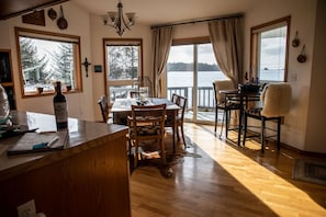 A cozy dining area with wooden furniture, a large window offering a view of a lake, and a rustic rug on the floor.