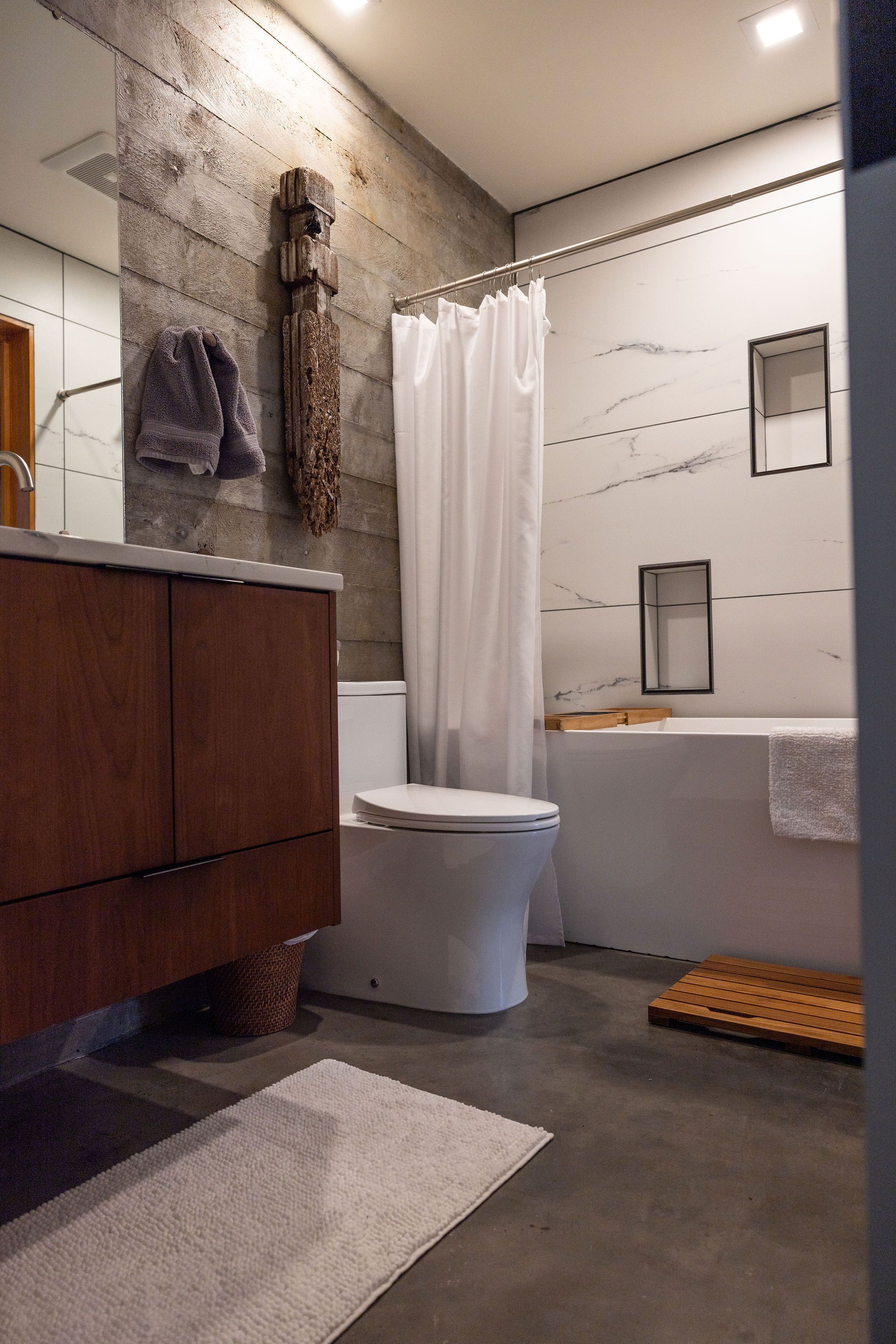 Ein modernes Badezimmer mit einem Holzkosmetikschrank, einer weißen Toilette und einer Marmorwand.
