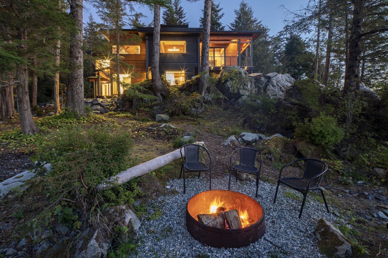 En moderne hytte med bålsted og udendørs siddepladser, omgivet af skov.