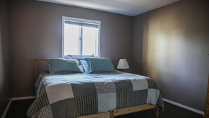 A single bed with a quilt, a window, and a lamp.