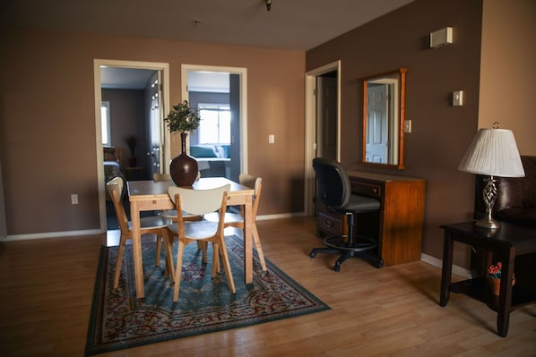 A living room with a dining table, chairs, a rug, a desk, a chair, a lamp, and a mirror. - Trierschield Bldg 23 (Sitka)