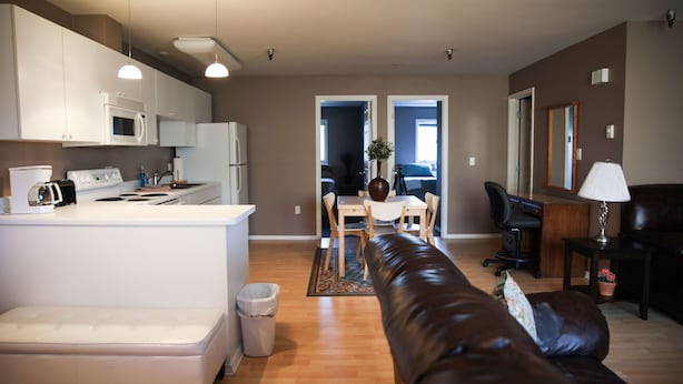 A modern kitchen with white appliances, a dining area with a table and chairs, a leather sofa, and a small side table with a lamp.