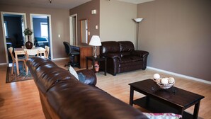 A living room with a brown leather sofa, a wooden coffee table, and a dining area with a table and chairs.