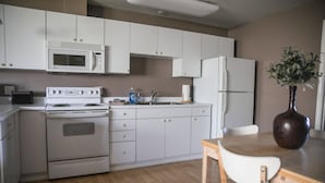A kitchen with white cabinets, a microwave, a stove, a sink, and a refrigerator. There is a vase with a plant on the dining table.