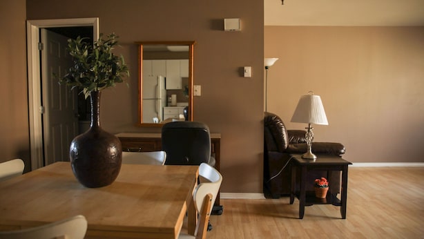 A dining area with a wooden table, chairs, a vase, and a mirror on the wall.