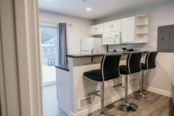 A modern kitchen with white cabinets, a black countertop, and three black bar stools.
