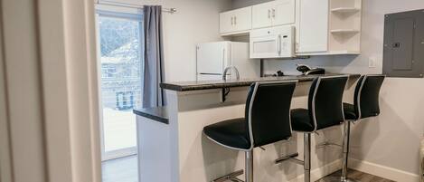 A modern kitchen with white cabinets, a black countertop, and three black bar stools.