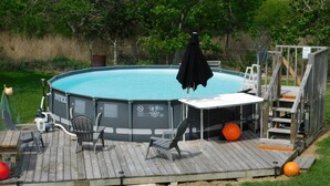 Una piscina elevada con una terraza, sillas de descanso y una pequeña mesa.
