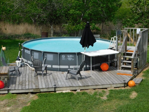 Ein überirdischer Swimmingpool mit Terrasse, Liegestühlen und einem kleinen Tisch.