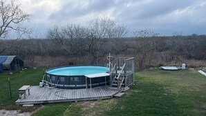 Una piscina con solárium, rodeada por un jardín cubierto de césped y árboles.
