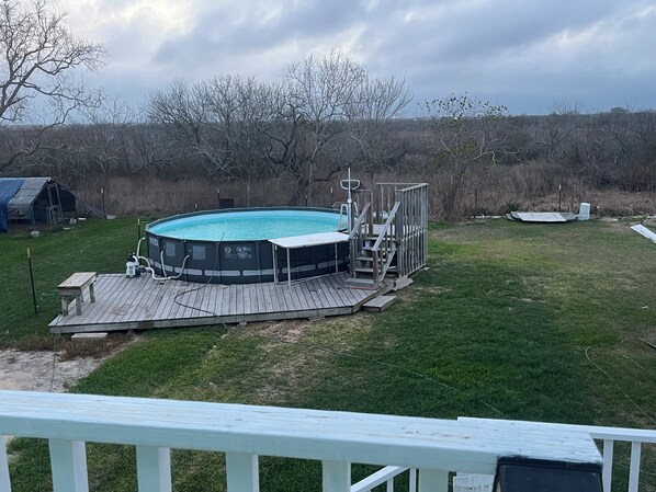 A swimming pool with a deck, surrounded by a grassy yard and trees. - Bay View Home with Pool near tranquil Carancahua Bay (Port Lavaca)