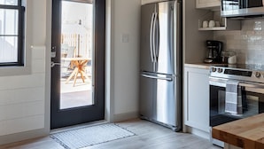 A modern kitchen with white cabinets, stainless steel appliances, and a view to the outside. - 3-East: Luxe 3BR in Downtown Nashville, IN w/ Rooftop Patio (Nashville)