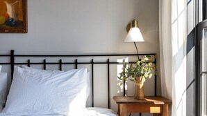 A neatly made bed with a blue comforter, a bedside table with a lamp and a vase of flowers, and a painting on the wall. - 3-East: Luxe 3BR in Downtown Nashville, IN w/ Rooftop Patio (Nashville)