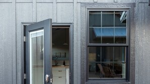 A modern building exterior with a glass door entrance, a small window, and a visible kitchen area inside. - 3-East: Luxe 3BR in Downtown Nashville, IN w/ Rooftop Patio (Nashville)