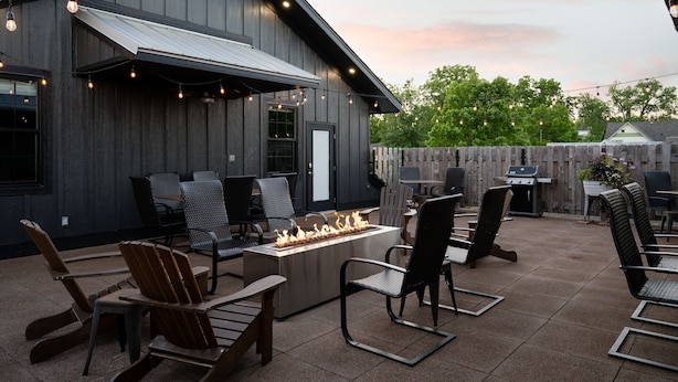 An outdoor patio with a fire feature, seating, and a building with a dark exterior. - 3-East: Luxe 3BR in Downtown Nashville, IN w/ Rooftop Patio (Nashville)