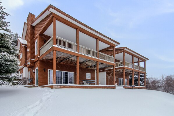 A two-story wooden house with a balcony, surrounded by snow.